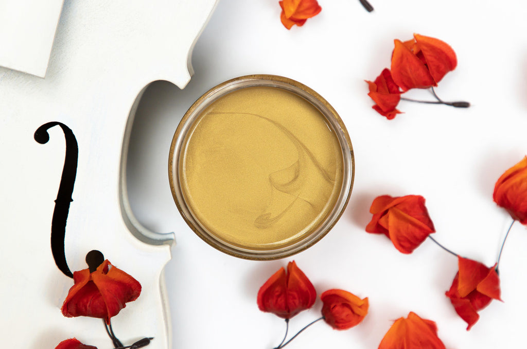 Open jar of Dixie Belle Moonshine Metallics paint in the color Gold Digger, with rose petals surrounding it.