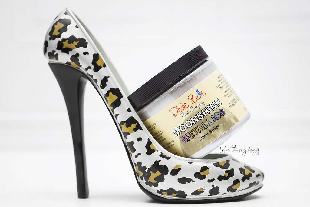 Dixie Belle Moonshine Metallics paint in the color Silver bullet. Paint can propped in a white gold black high heeled shoe.