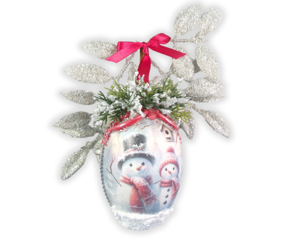 Two snowman in hats and scarves decoupage onto plastic egg shaped ornament with greenery and red bow.