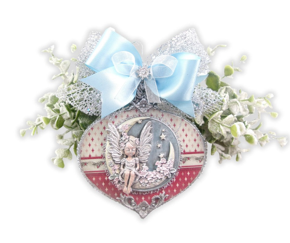 Moon angel ornament with clay figure on a crescent, red-white rice paper, silver trim, blue bow, on snowy evergreen.