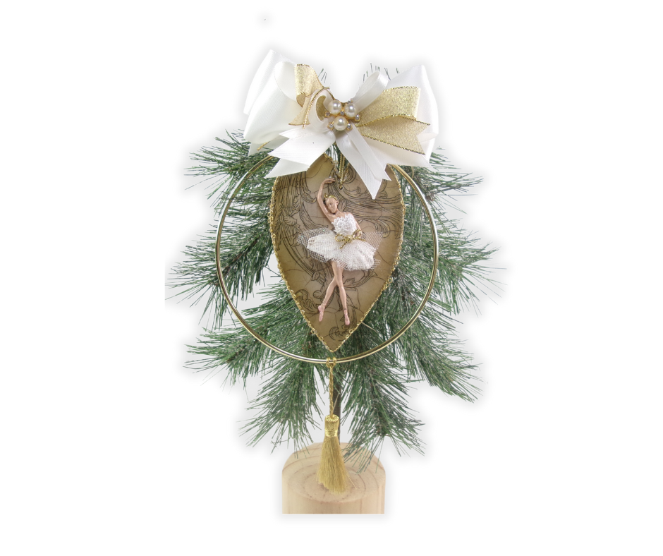 Heart-shaped Christmas ornament with a clay ballerina inside a gold ring, topped with a white-and-gold bow and gold tassel.