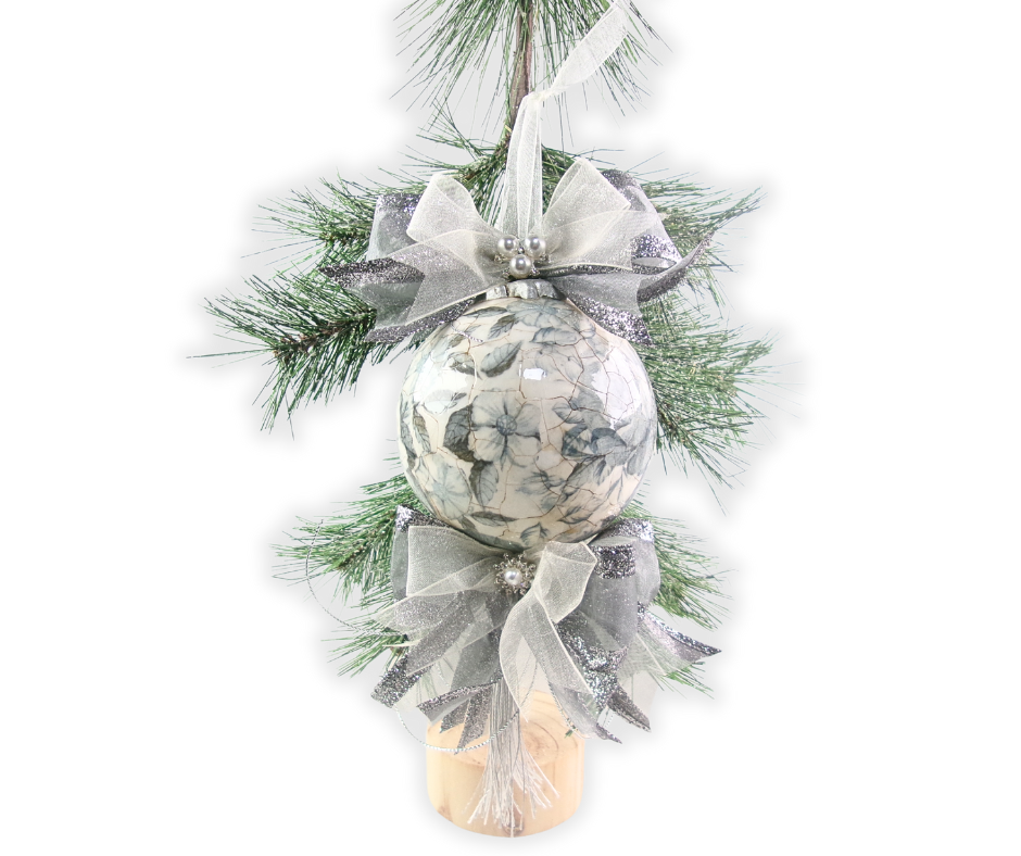 Handmade porcelain-style Christmas ornament with blue floral decoupage, fine crackle finish, silver ribbons, and pearl accents displayed on evergreen branches.