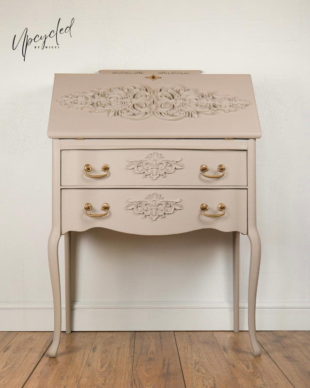 Upcycled furniture piece with floral carvings on a wooden floor and white wall background.