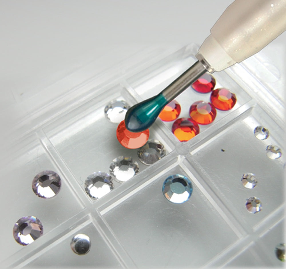 Tool with a green handle picking up colorful gemstones from a grid.