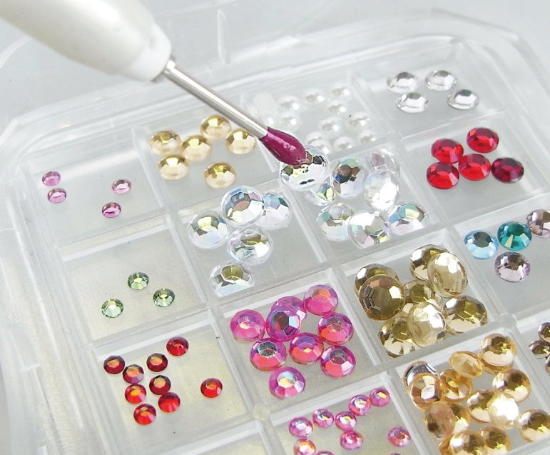 Assorted gemstones in a clear plastic organizer with a small tool.