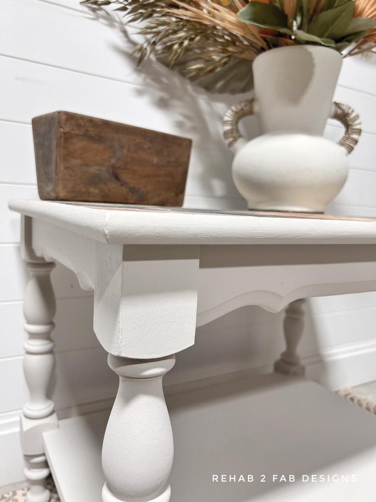 White table with decorative items against a white wall, featuring the brand 'Rehab 2 Fab Designs'.
