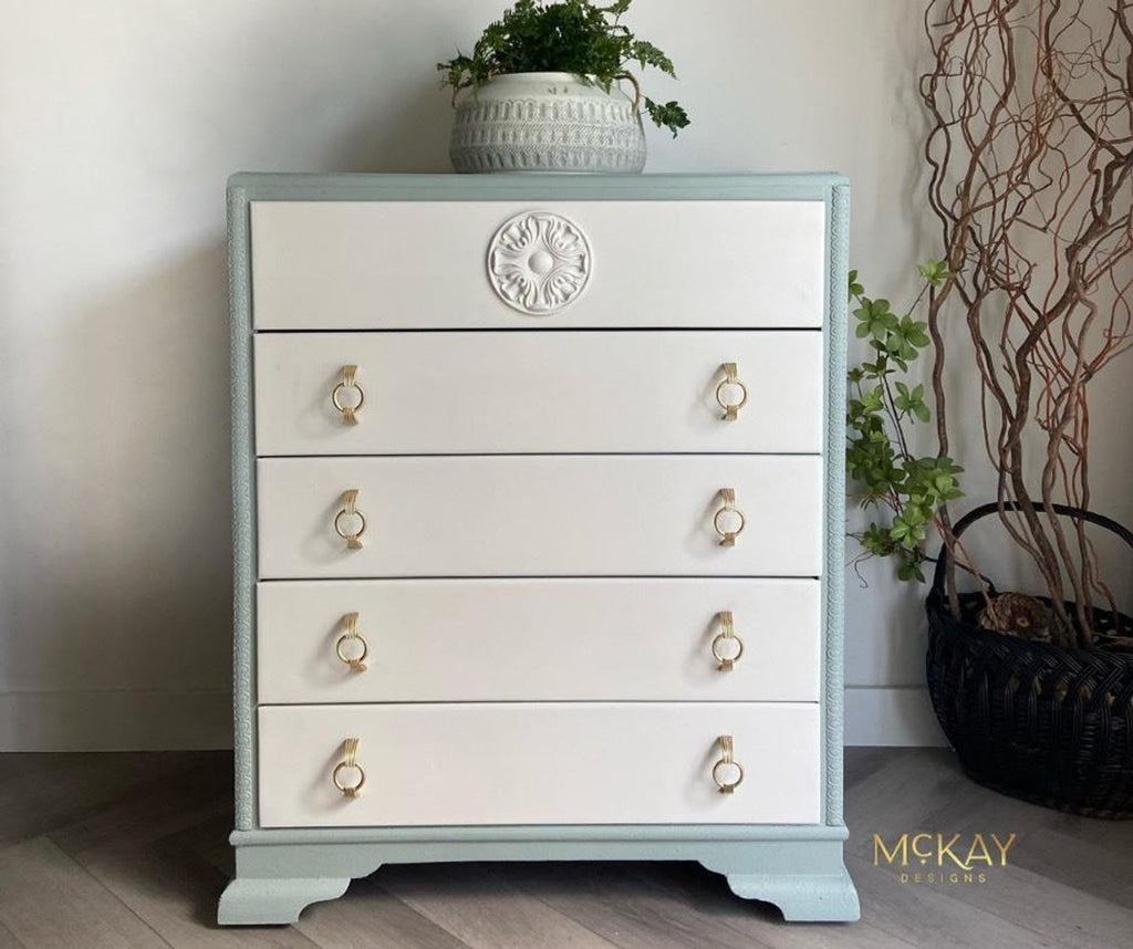 White dresser with gold knobs against a neutral wall with decorative elements.
