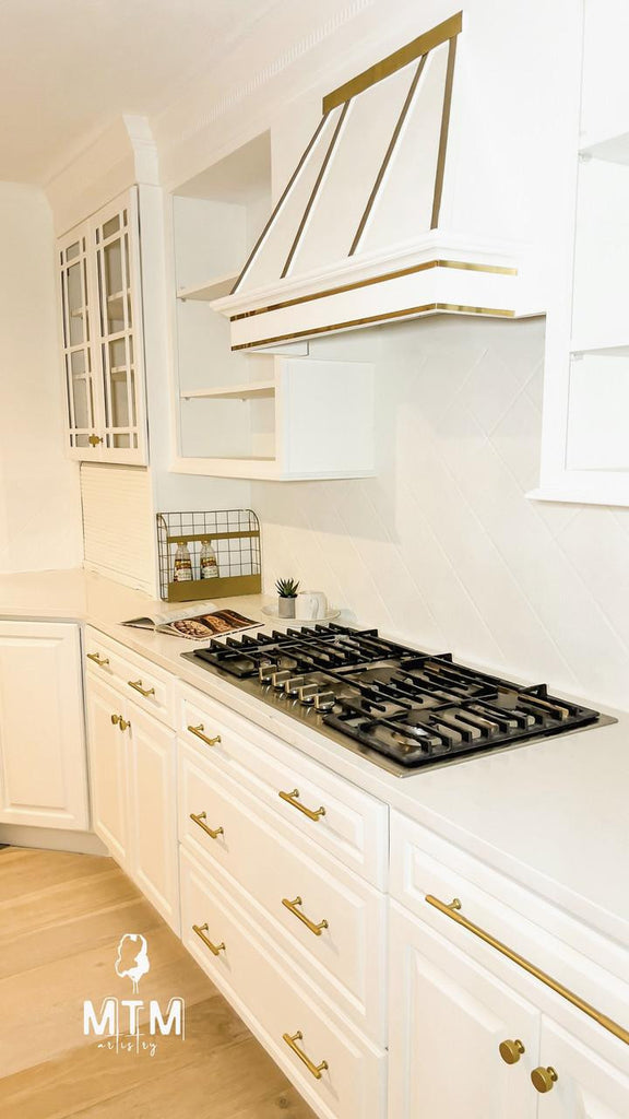 Modern kitchen with white cabinets, gold handles, and a black stovetop.