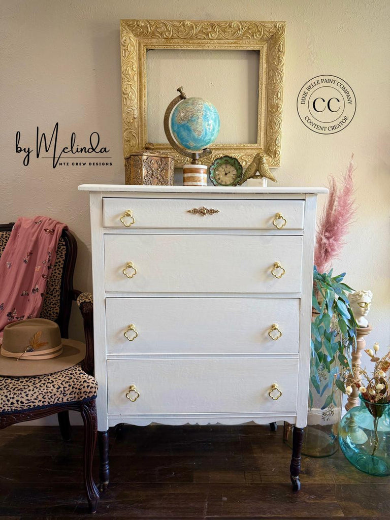 White dresser with gold knobs in a room with a chair, globe, and decorative items.