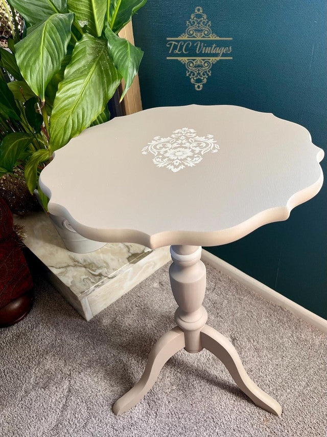Small round table with decorative stenciling on a carpeted floor, with 'TLC Vintage' branding in the background.