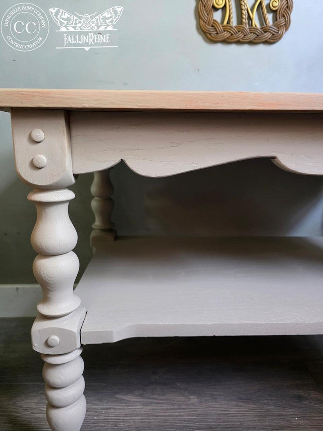 Wooden table with white painted base and light wood top, featuring a visible brand logo.