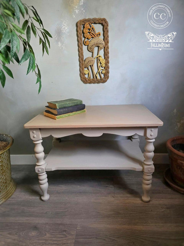 Wooden table with books and a decorative wall piece on a wooden floor.