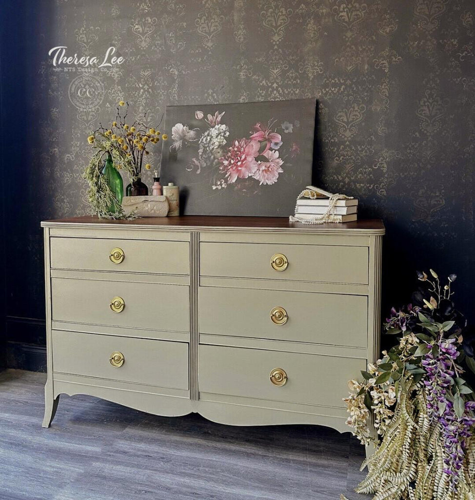 Vintage-style dresser with gold knobs against a dark wall, featuring decorative elements.