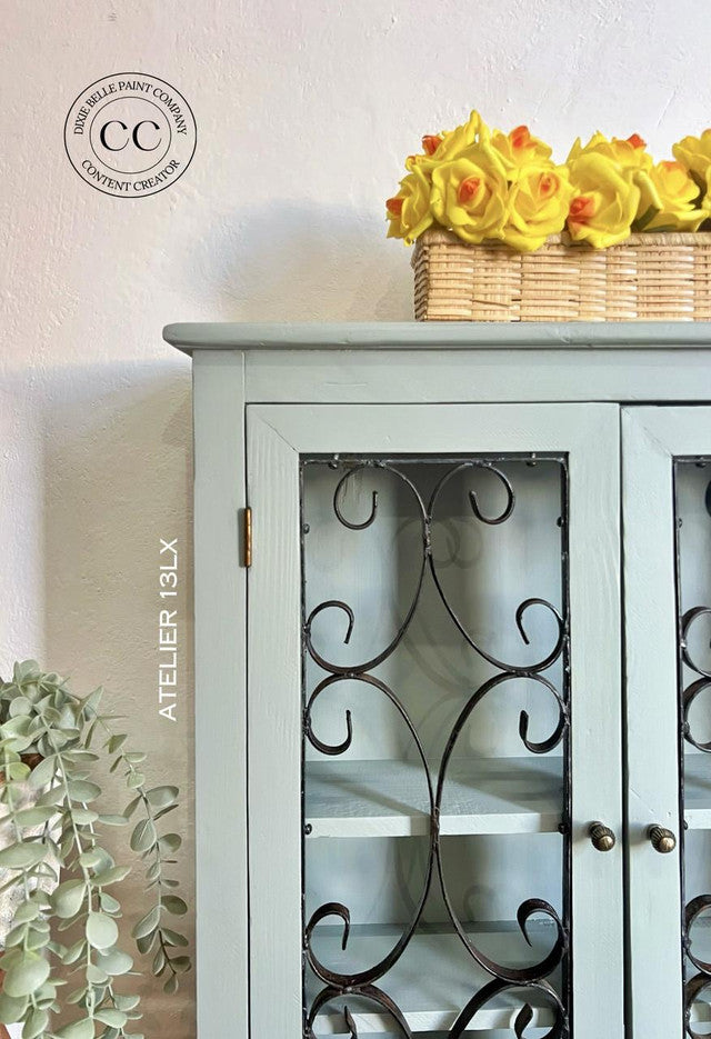 Light blue cabinet with decorative glass doors and a basket of yellow flowers on top.