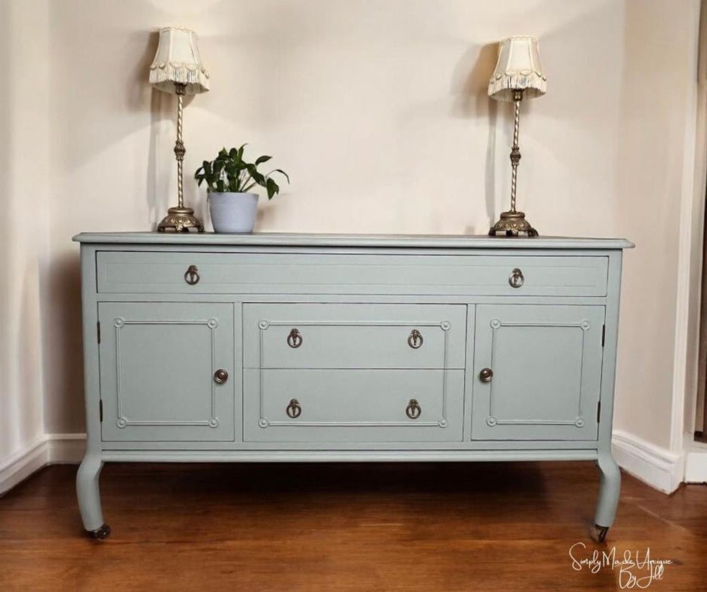 Light blue sideboard with two lamps and a plant on top against a white wall.