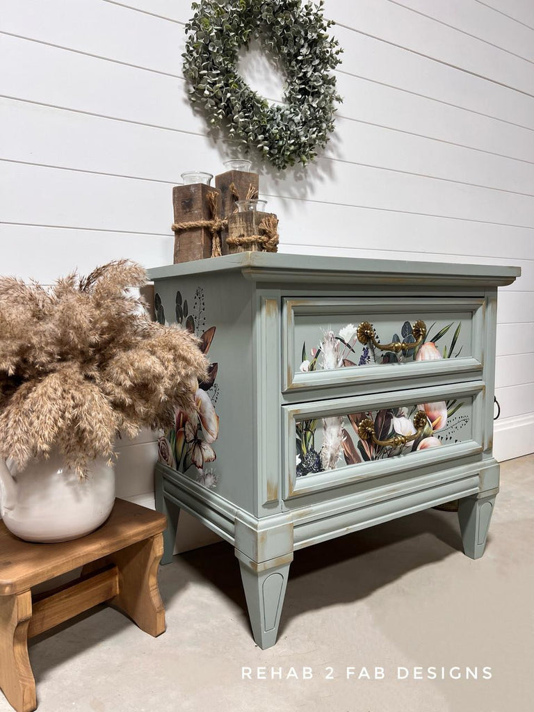 Light blue distressed nightstand with decorative items against a white wall, featuring 'Rehab 2 Fab Designs' branding.