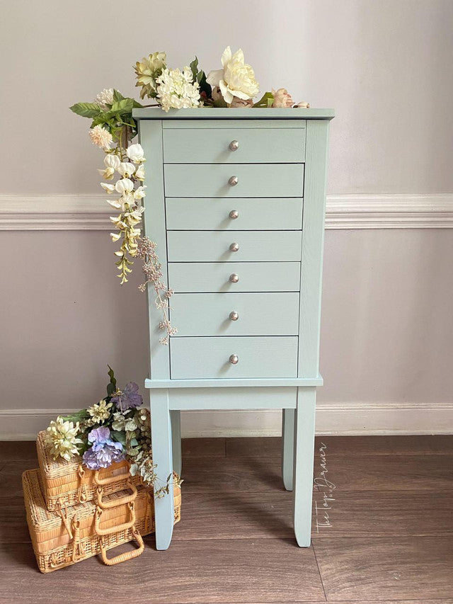 Light blue jewelry armoire with floral decorations on a wooden floor.