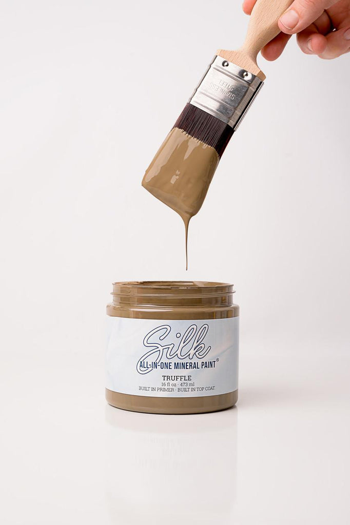 Jar of Silk All-In-One Mineral Paint with a brush dipping into it on a white background