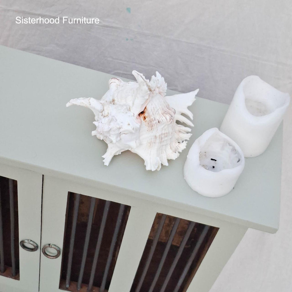 Seashell and two white candles on a light green surface with 'Sisterhood Furniture' branding.